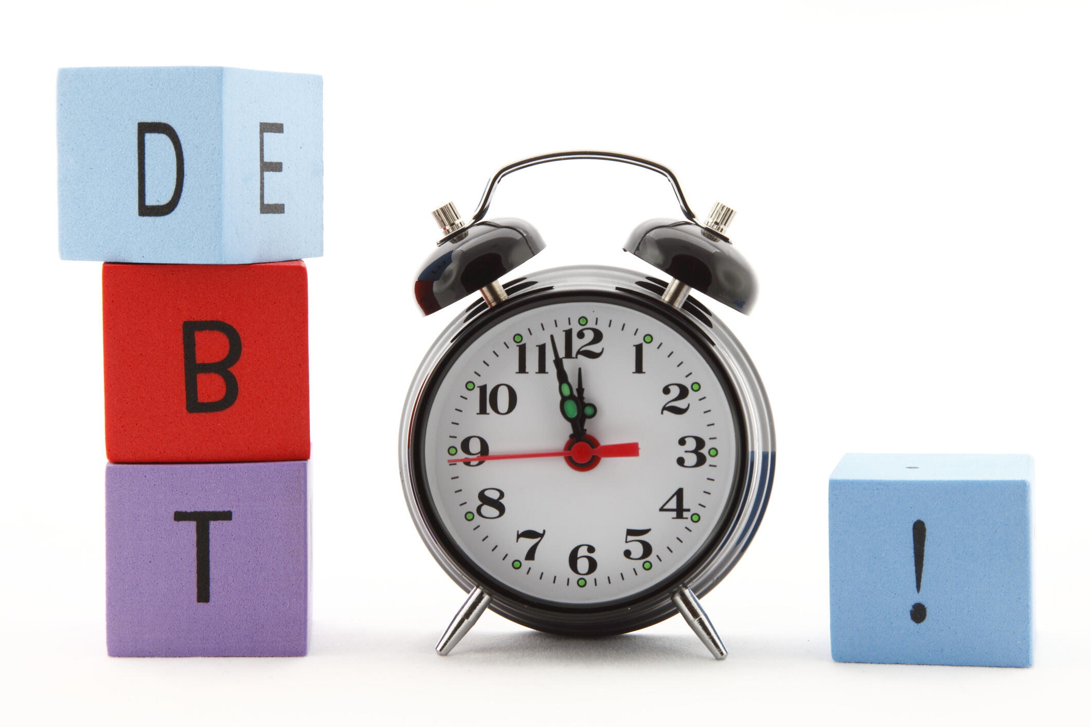 A photo of an alarm clock with multicolored building blocks on either side of it. The three blocks on the left side spell out 