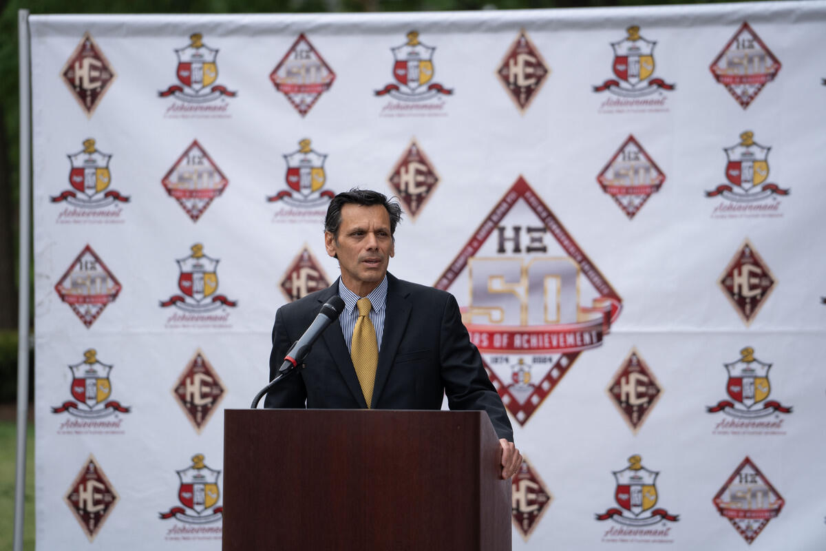 A photo of a man standing behind a podium with a microphone