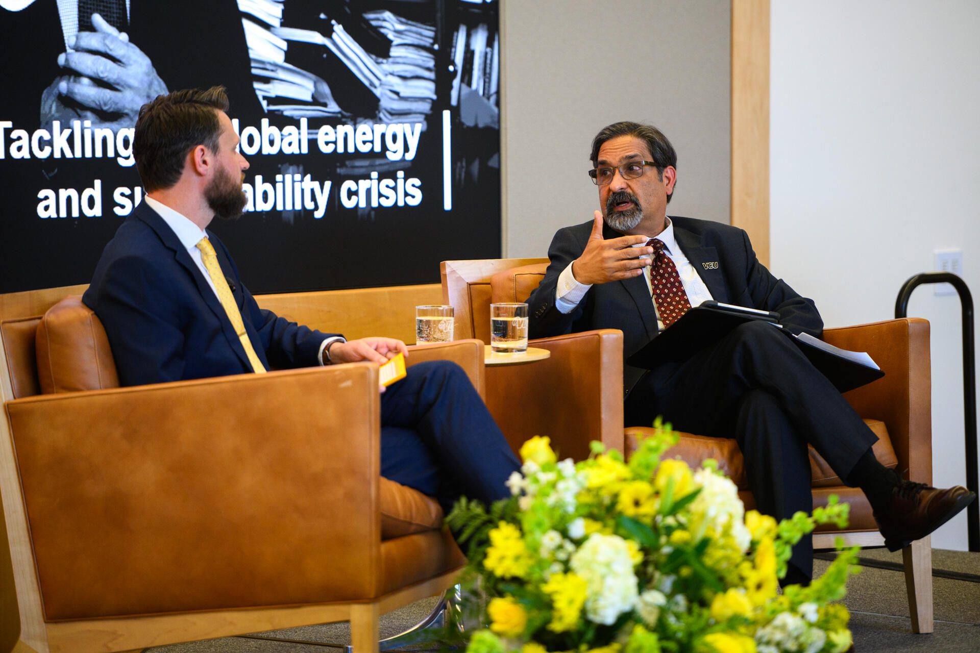 A photo of two men sitting in brown arm chairs and talking. 
