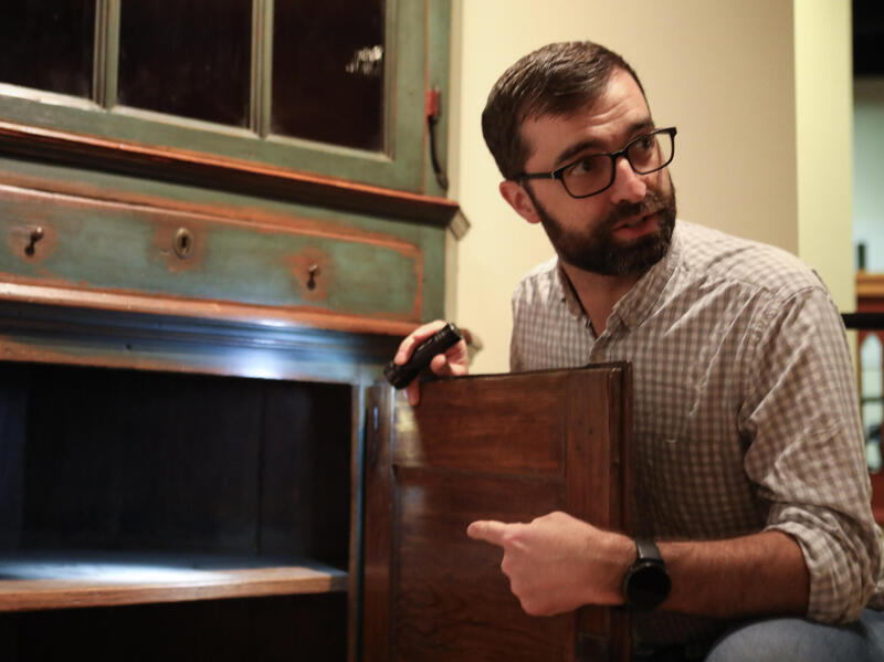 A photo of a man kneeling next to an old cupboard. 
