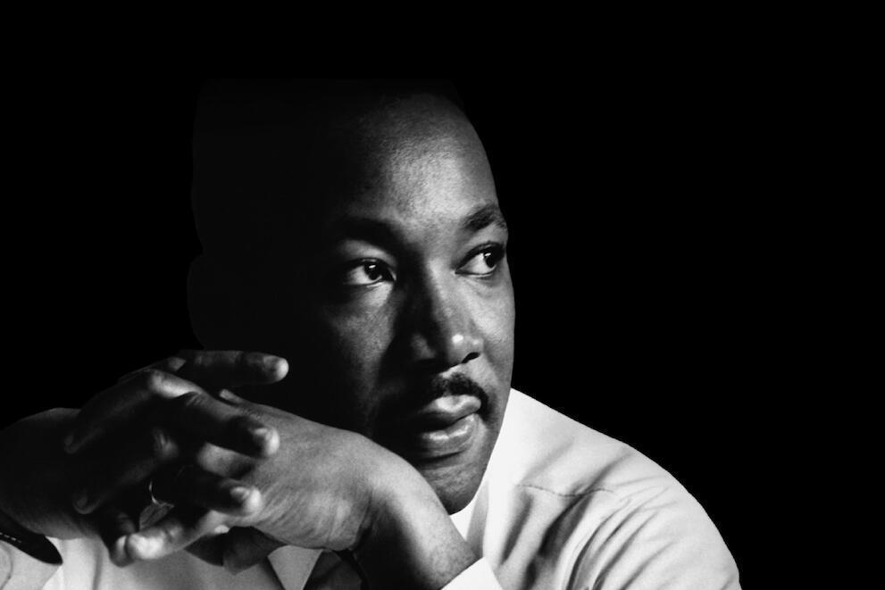 A black and white photo of Martin Luther King Jr. looking to the left with his hands in front of his face. 