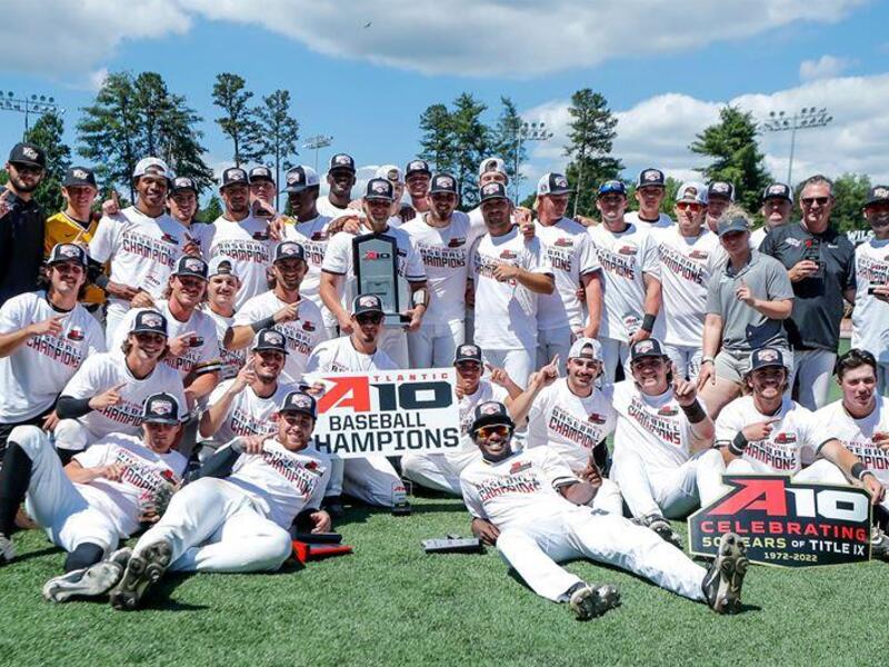 VCU's baseball team on a field with signs that says \"A10 BASEBALL CHAMPIONS\" 