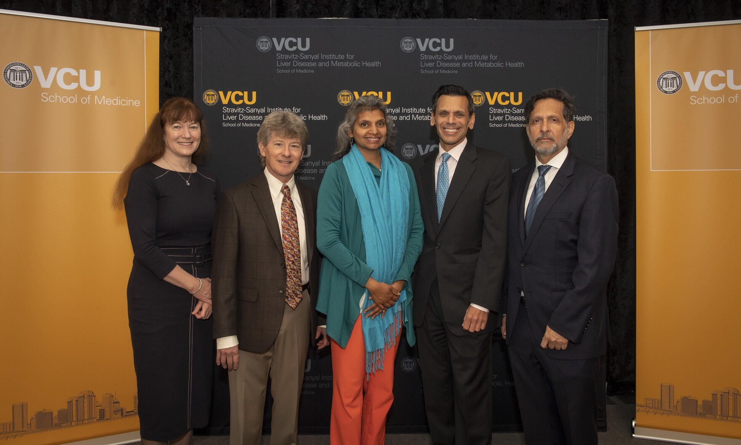 Five people standing in front of banners that say \"VCU.\"