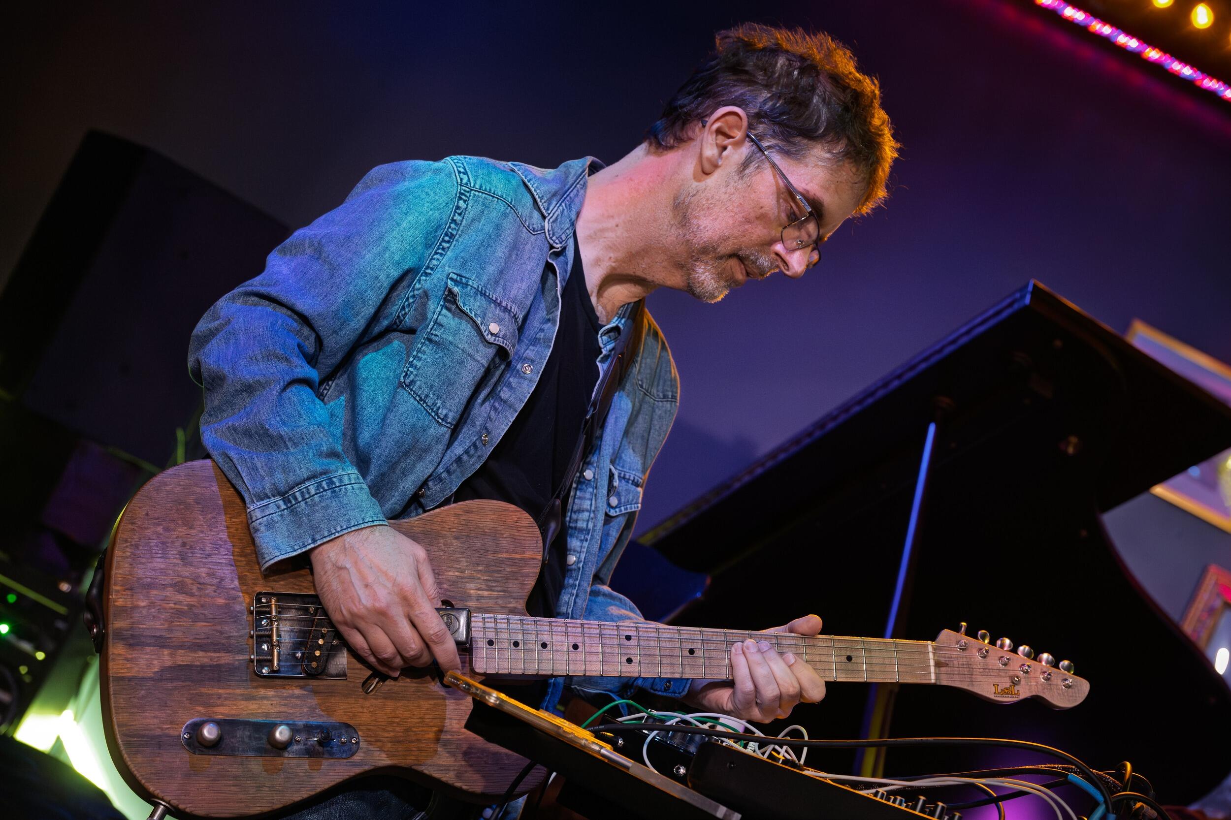 A photo of a man playing a wooden electric base guitar