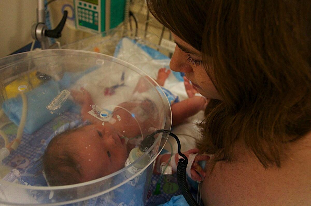A photo of a woman looking at a baby laying in an incubator. 