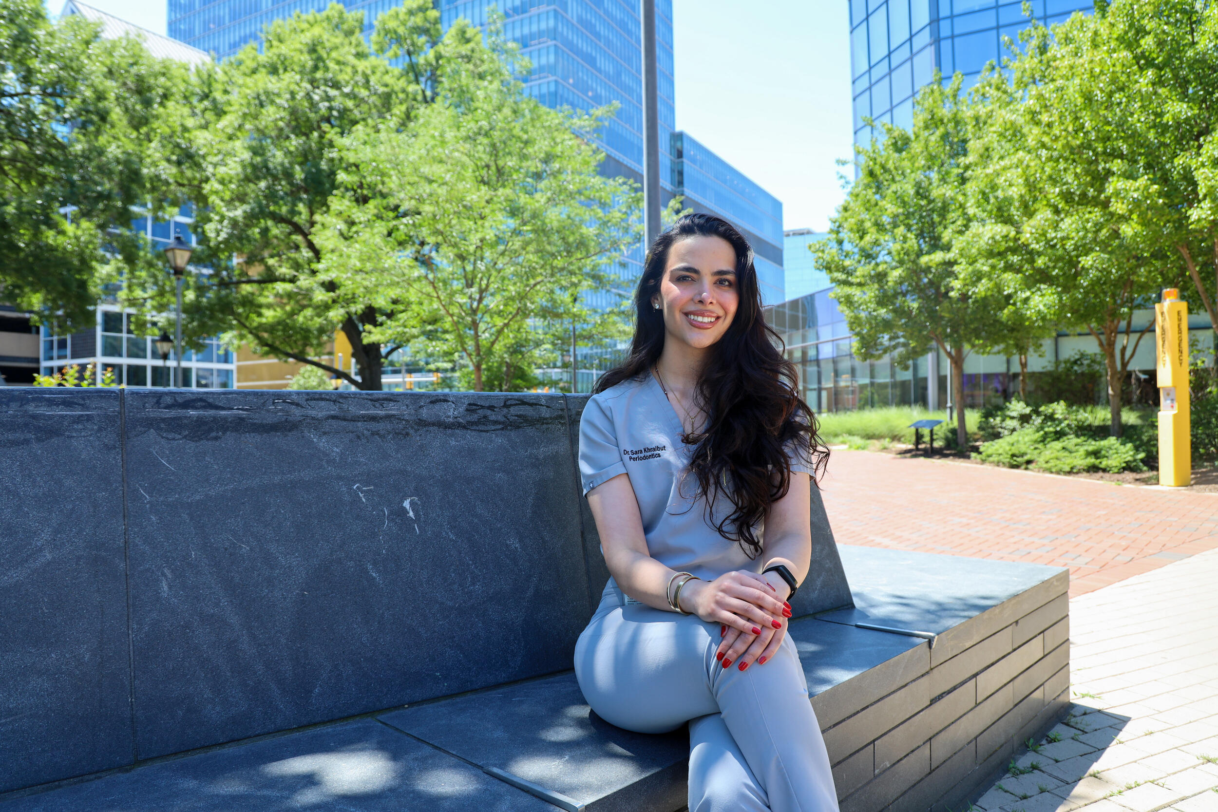 A photo of a woman sitting on a stone bench outside. 