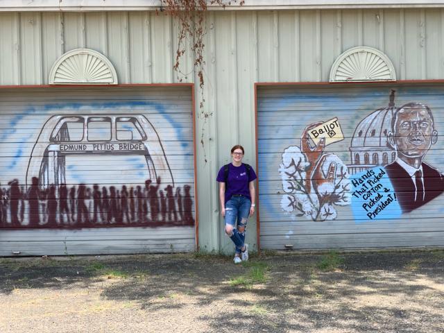 VCU student Jordan Moye in front of two rusting garage doors with murals depicting the Edmund Pettus Bridge and the movement for voting rights