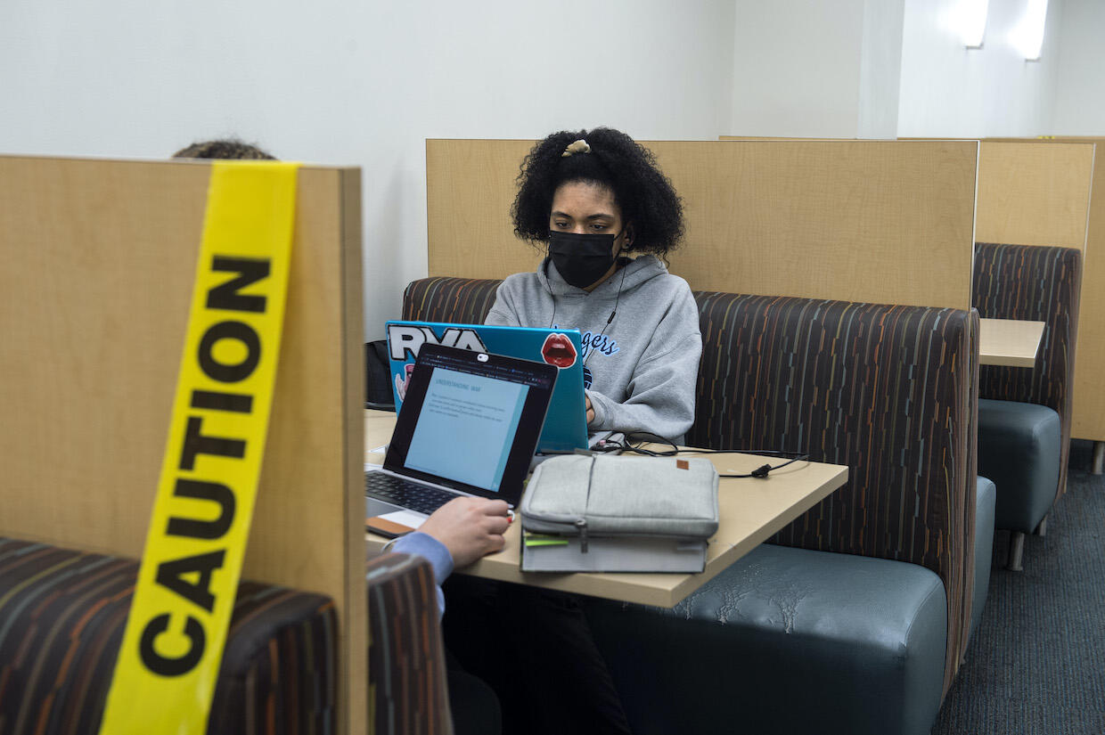 Two students sit in a booth at Cabell Library. Caution tape cordons off the closest booth from being occupied.
