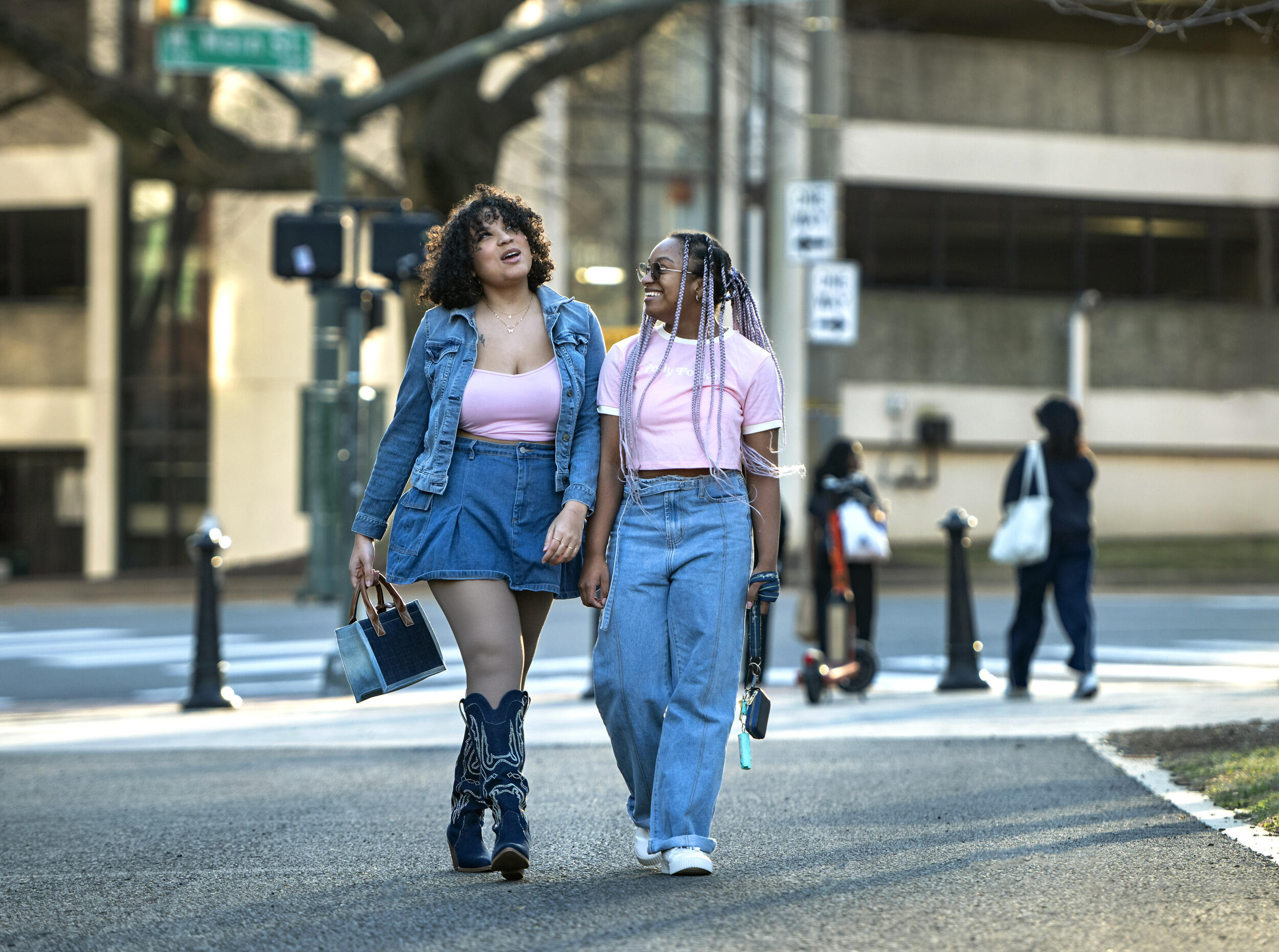 A photo of two women walking next to each other down a sidewalk. 