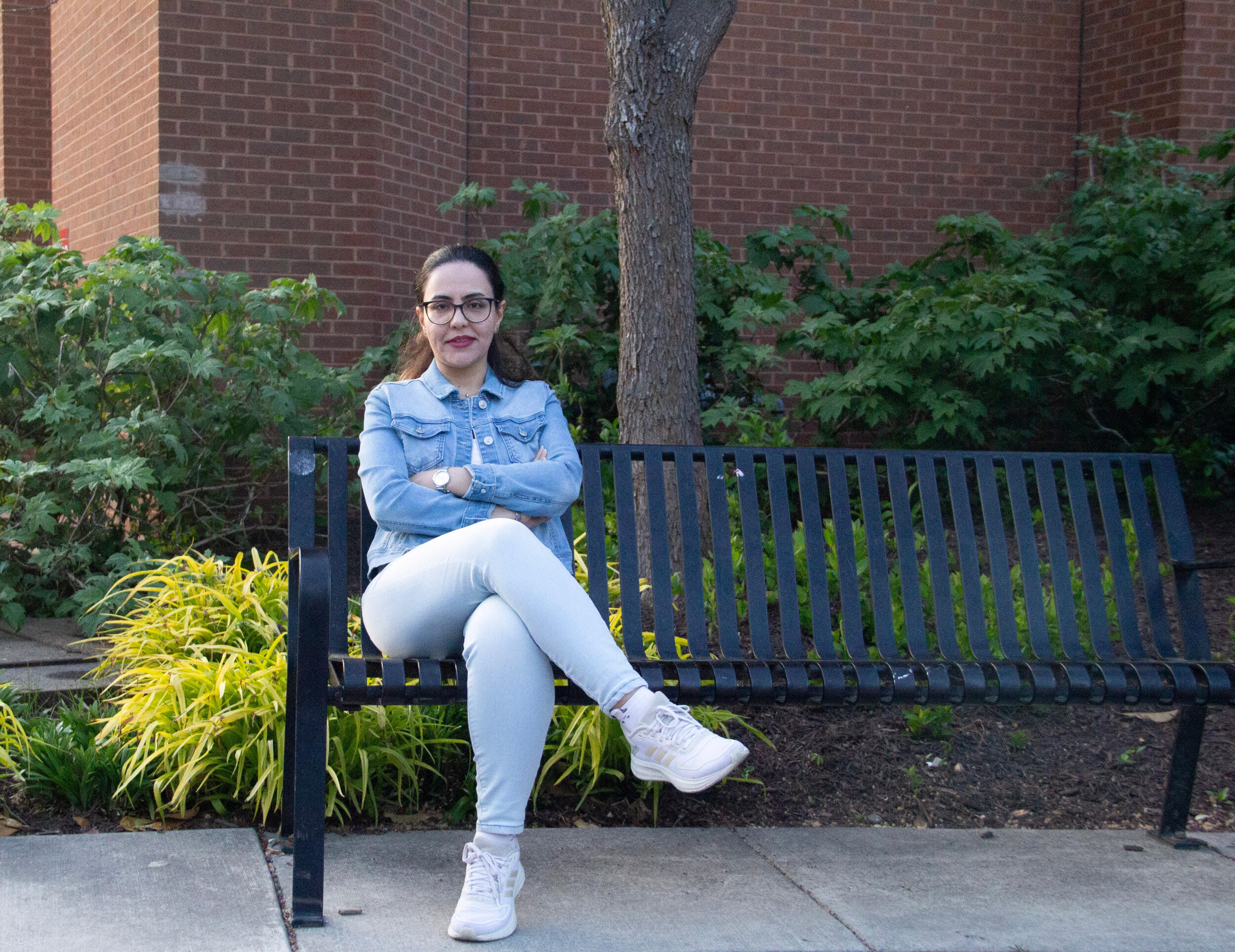 A woman sits on a bench with her legs crossed.