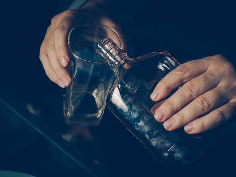 A person pours a drink from a glass bottle.
