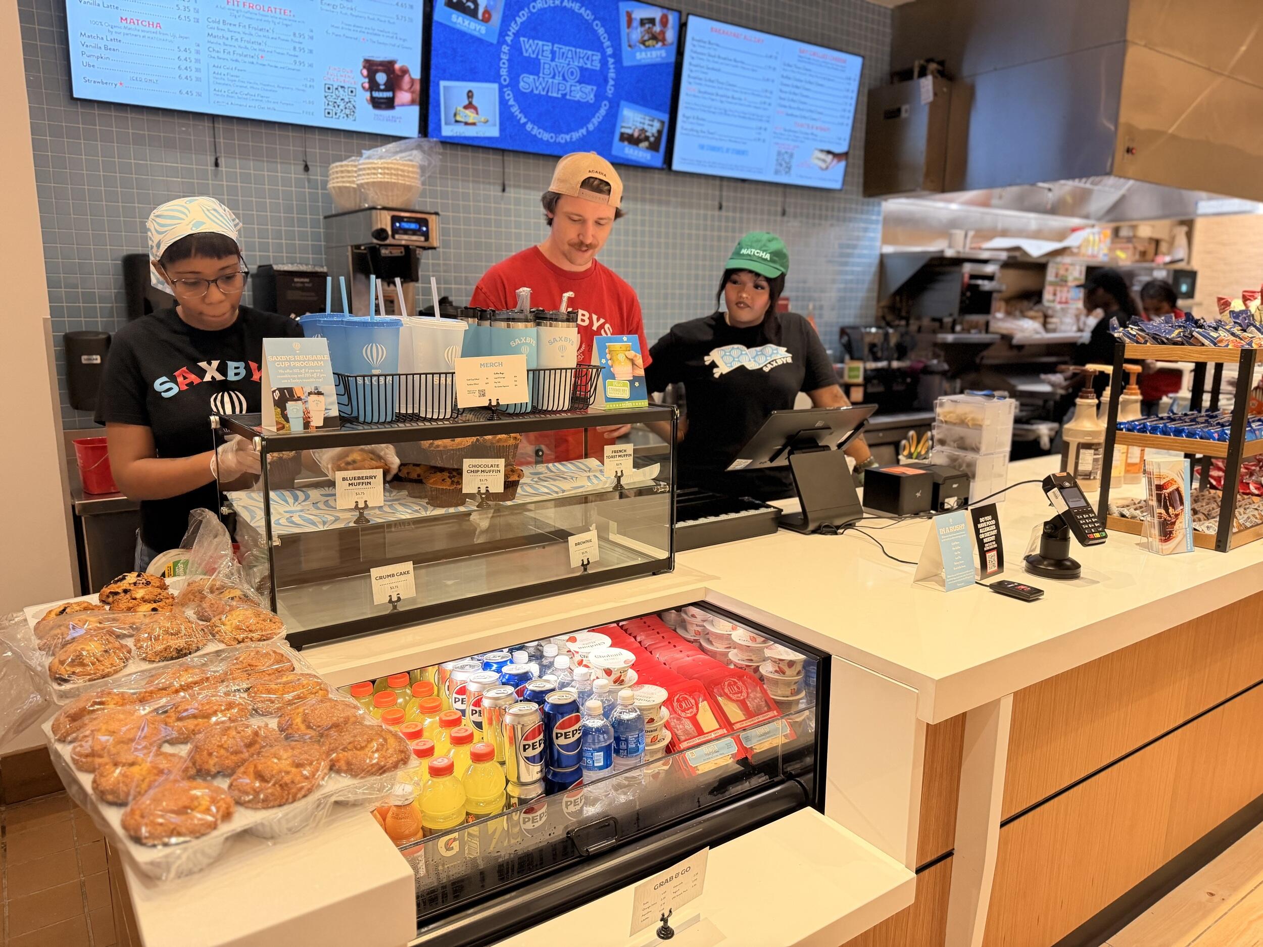 A photo of three people standing behind a coffee shop counter. 