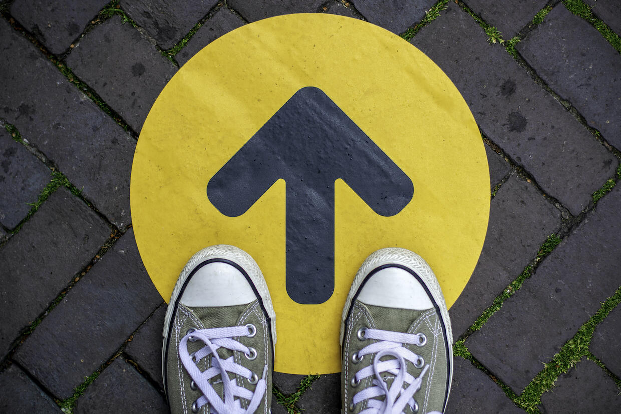 A pair of shoes standing on a dot with an arrow pointing forward.