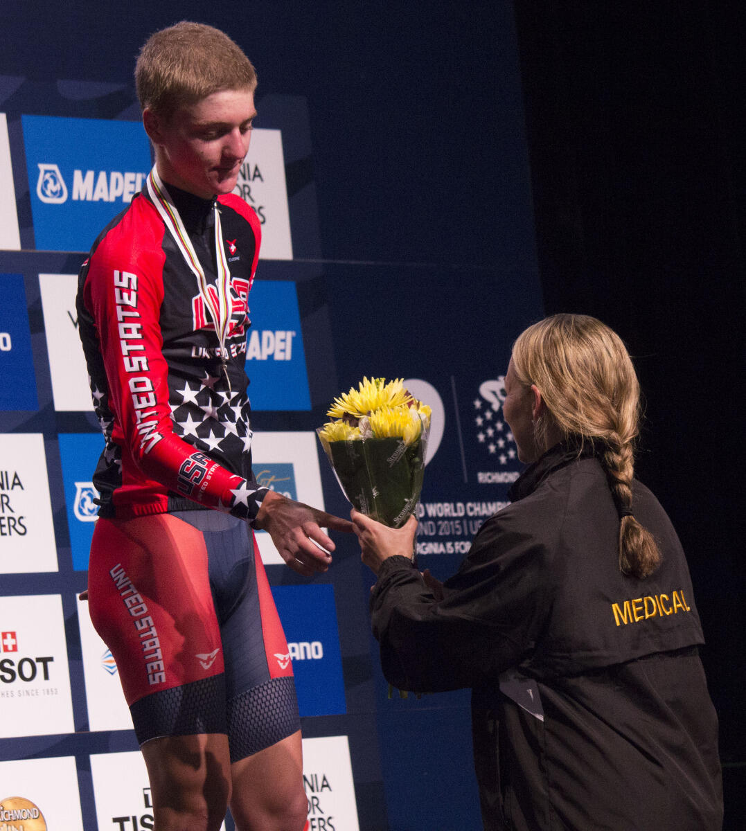 Rebecca Moran, D.P.T., hands flowers to Adrien Costa, a USA cyclist, during the medal ceremony for the men’s junior individual time trial. Costa came in second place.