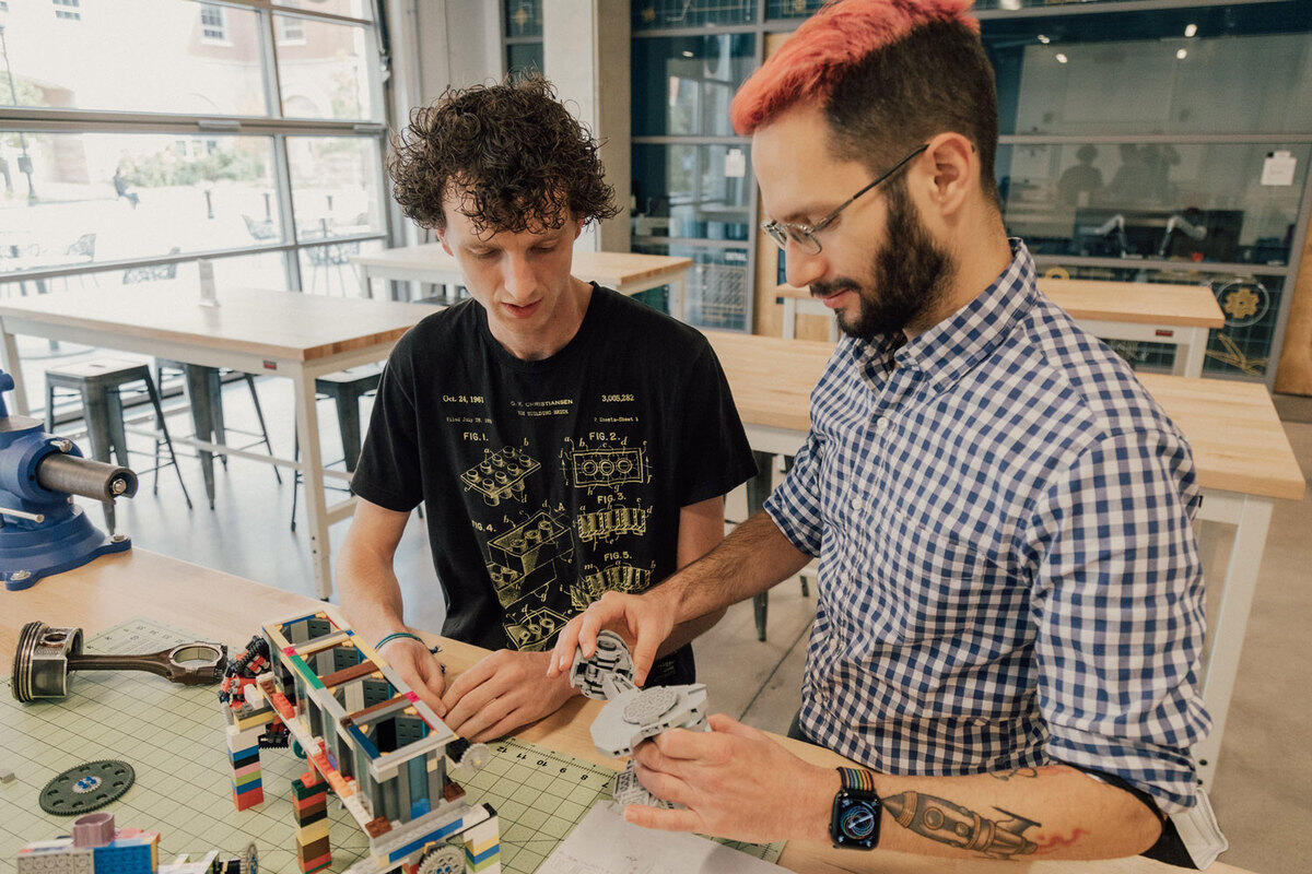 Two men sitting at a table building a lego structure 
