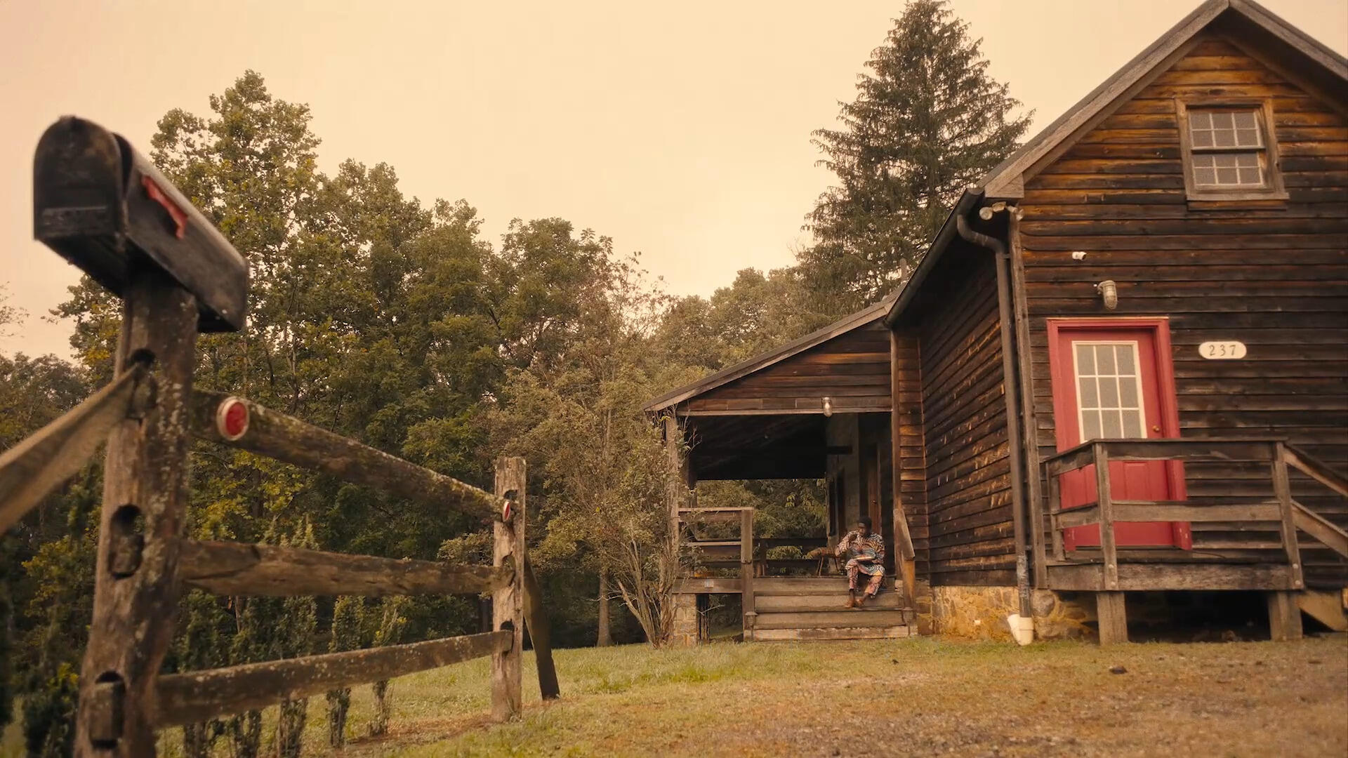 A man sitting on the porch of a cabin in front of the woods 