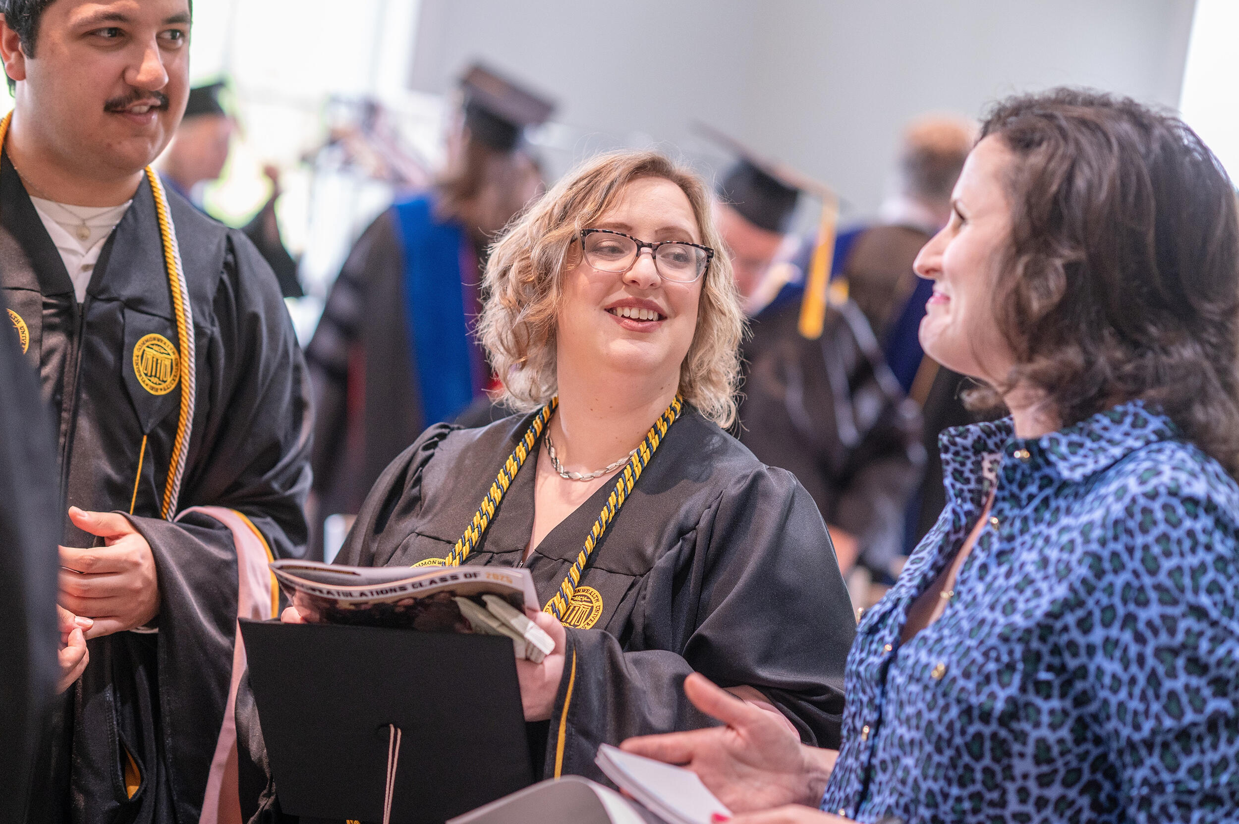 A photo of three people. The two people on the left are wearing college graduation gowns. 