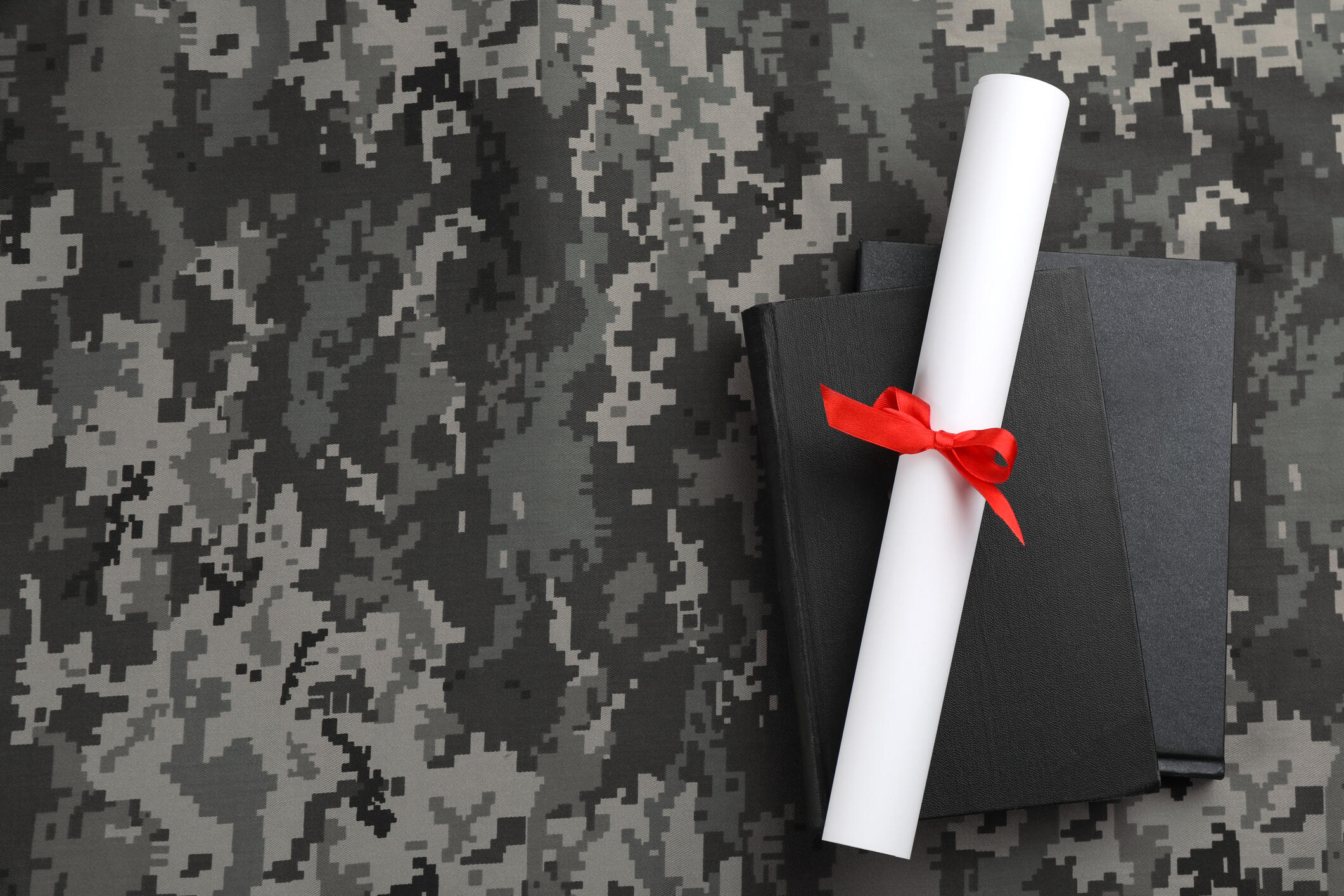 Camouflage background with books and a rolled diploma.