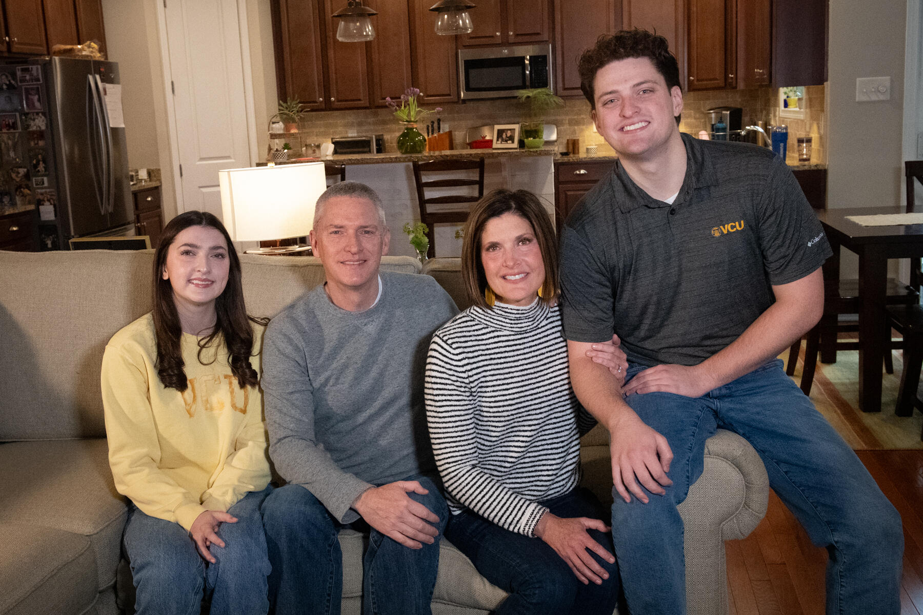 A photo of four people sitting on a couch. To the far left is a girl, to her right is a man, to the man's right is a woman, and to the far right is another man. 