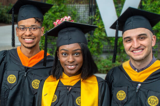 A group of three people in graduation attire, all smiling.
