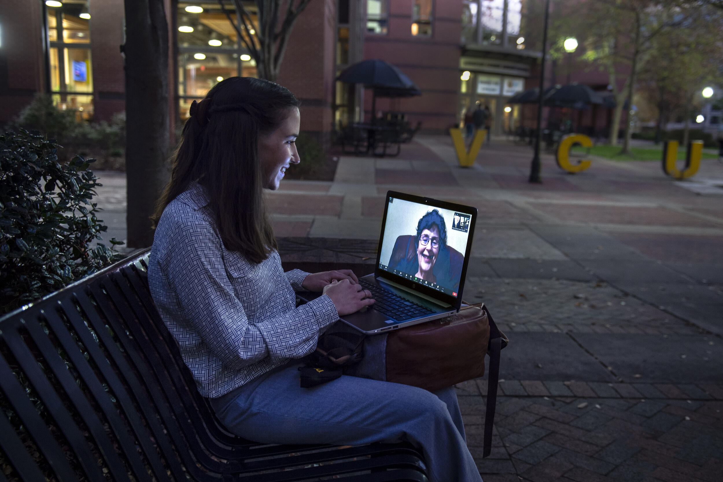 A student participates in a videoconference with a person while seated on a bench near near the Shafer Court Dining Center.