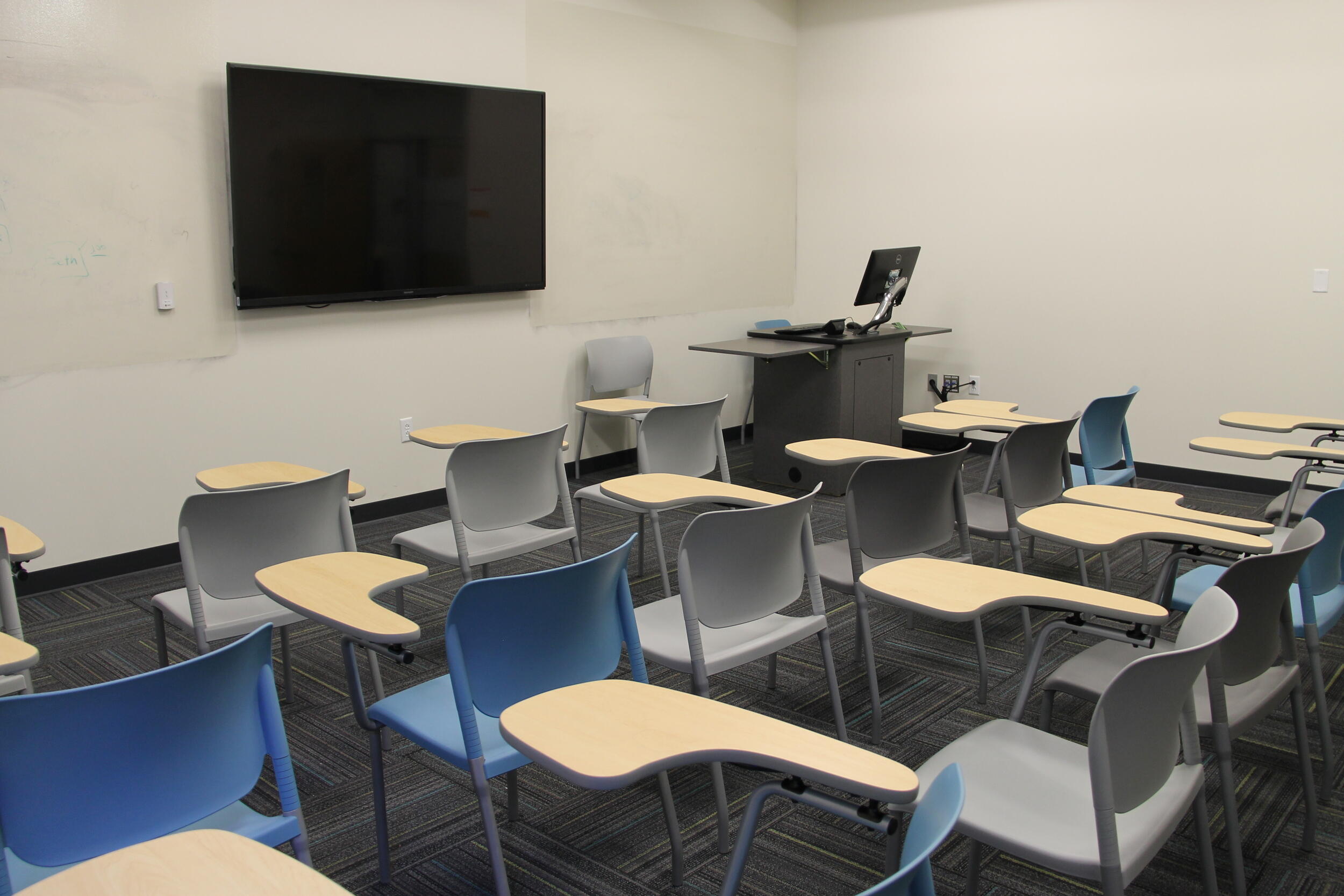 An empty classroom with desks facing a wall with a flatscreen TV on it 