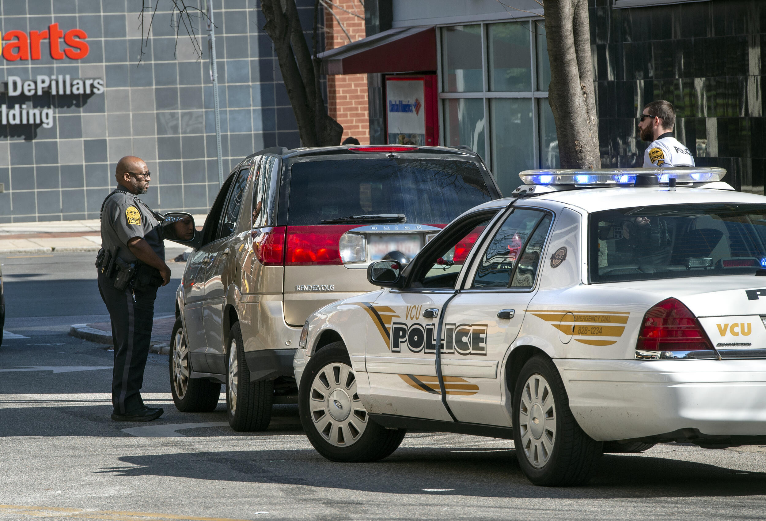 A police car parked behind an SUV. A police officer is standing next to the driver's window of the SUV.
