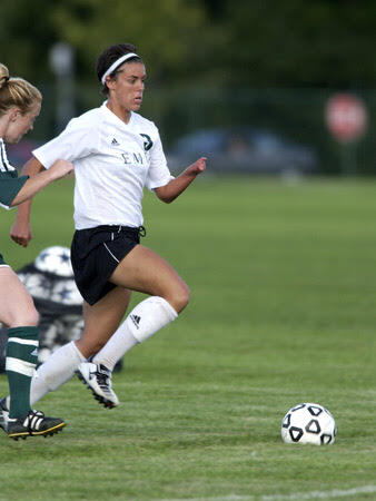 A photo of two women running on a soccer field, chasing after a ball. 