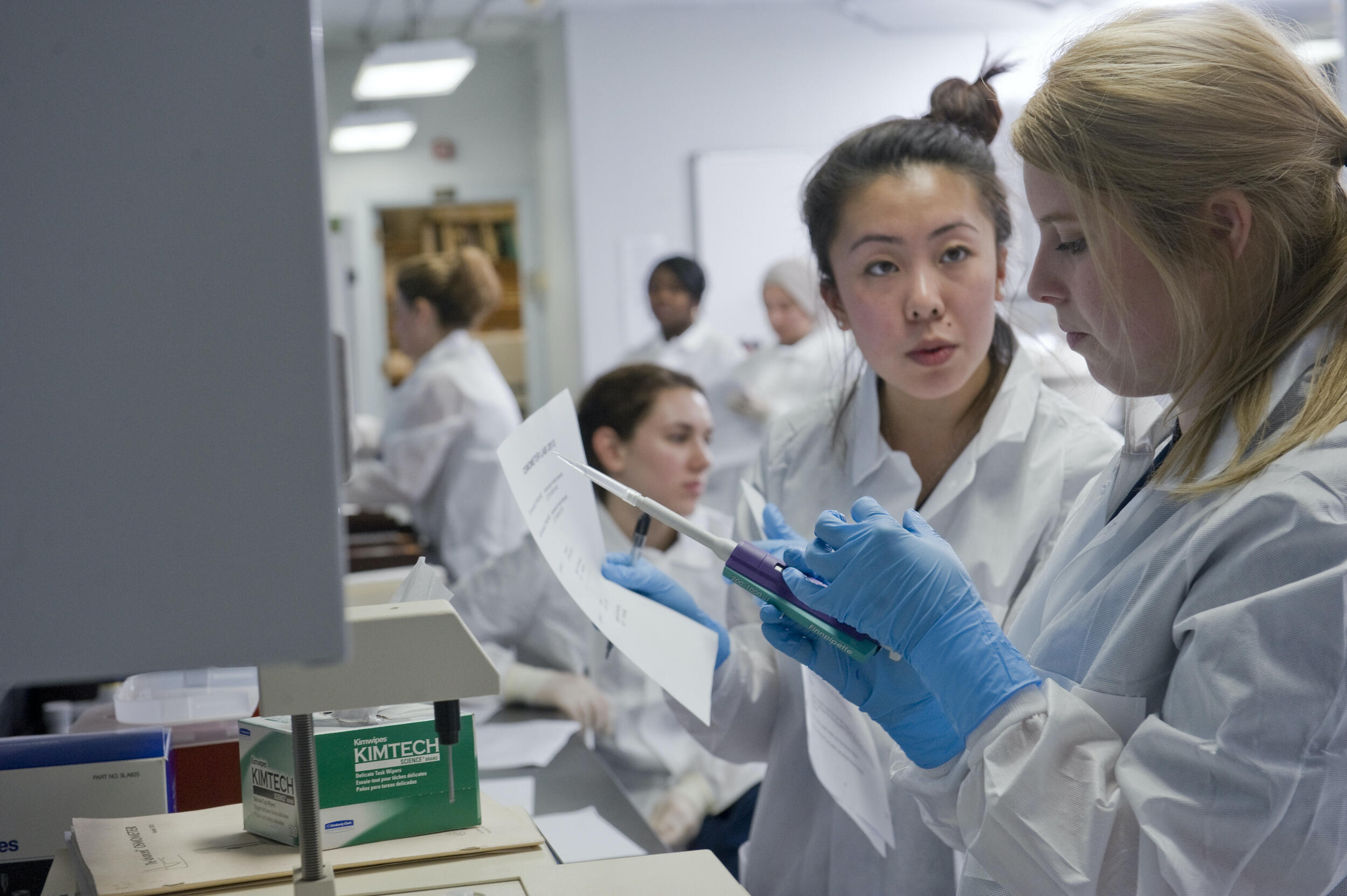 Women wearing lab coats and gloves in a research lab. 
