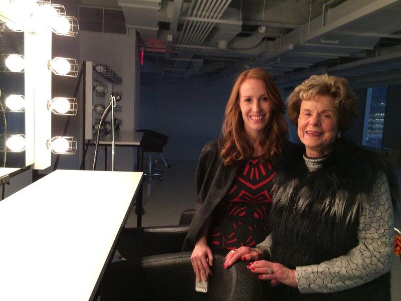 Two women pose in front of a dressing table.