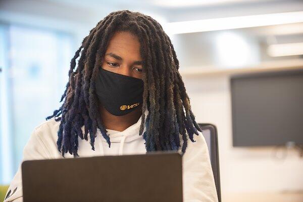 Photo of a student in a mask working on a laptop.
