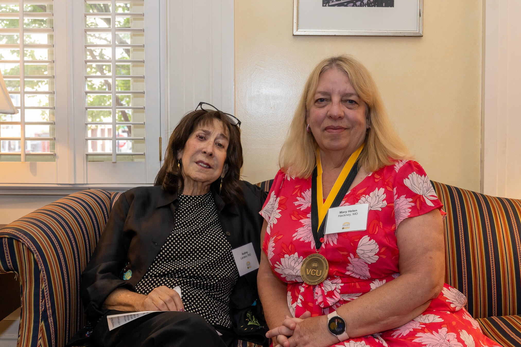 Two women sitting on a couch. The woman on the right is wearing a gold medal around her neck. 