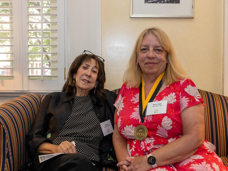 Two women sitting on a couch. The woman on the right is wearing a gold medal around her neck. 
