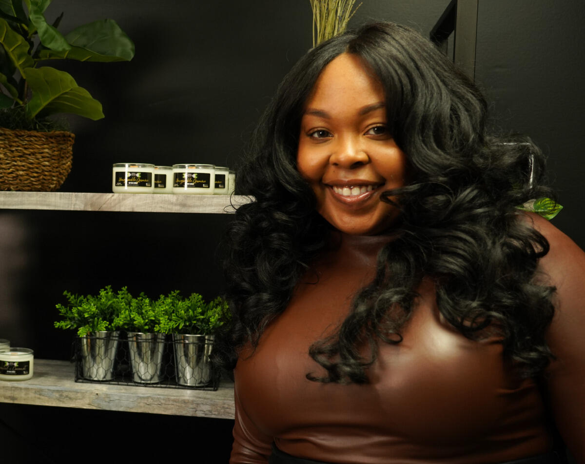 A woman with long curly black hair standing next to shelves that have plants on them. 