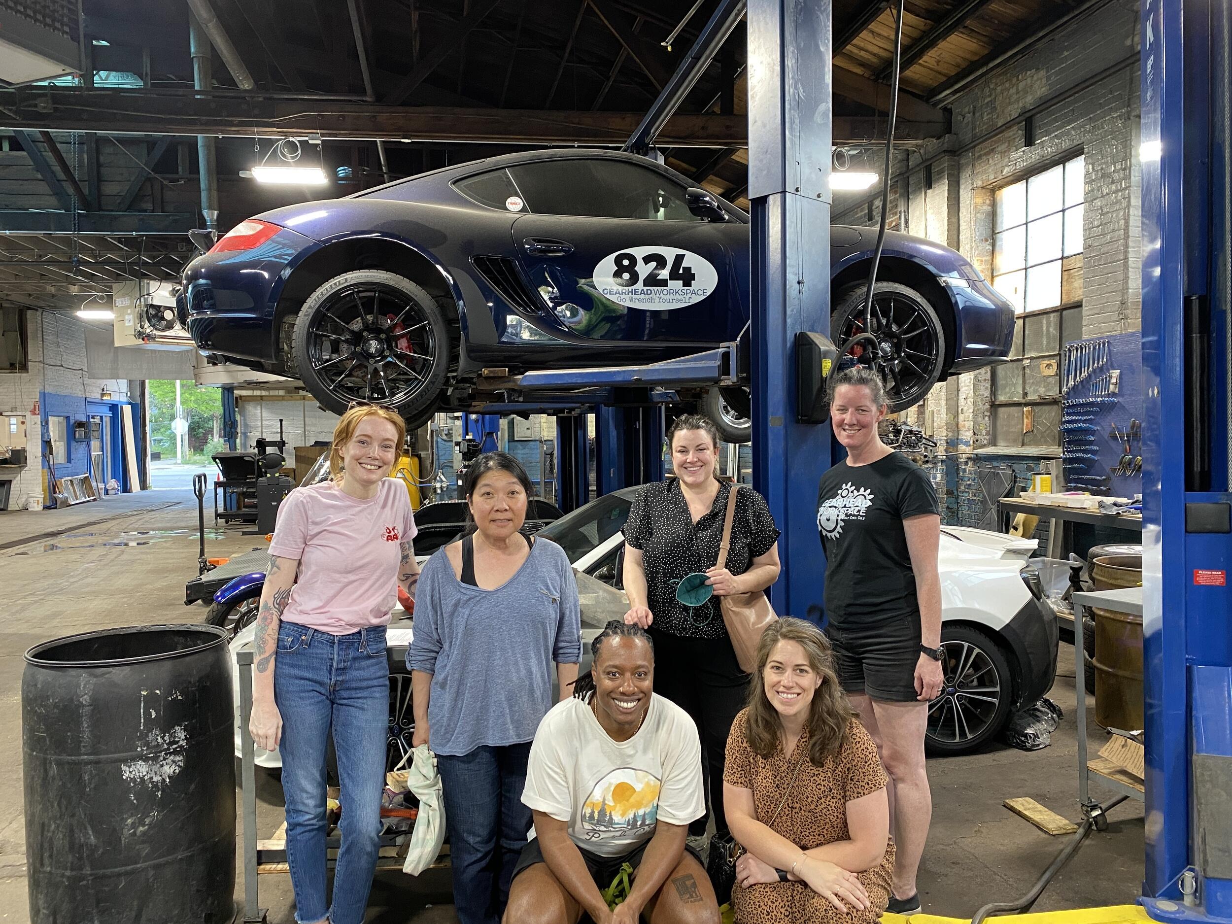 Six women standing in front of a car in a garage 