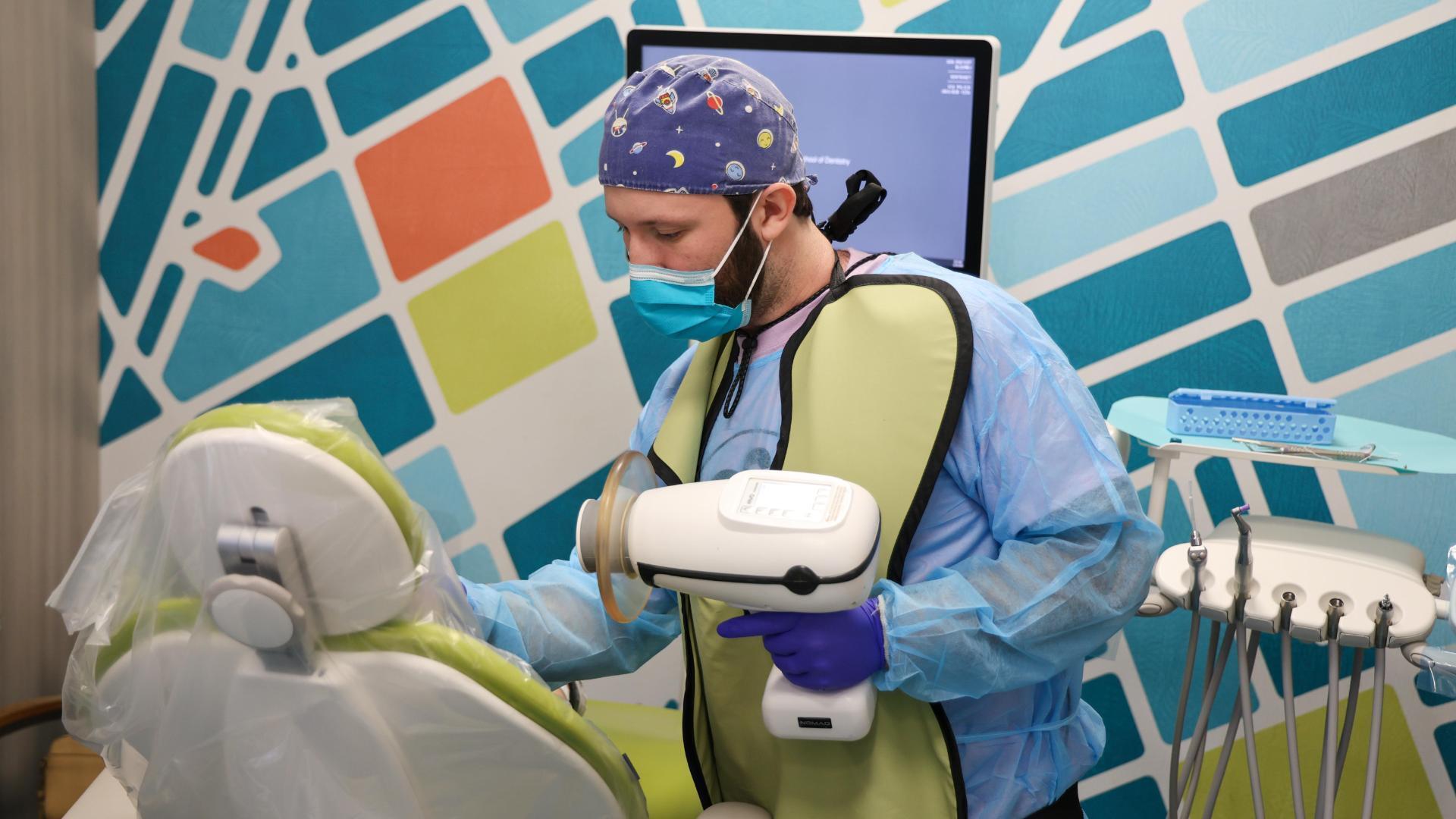 A photo of a man standing next to a dental chair. 