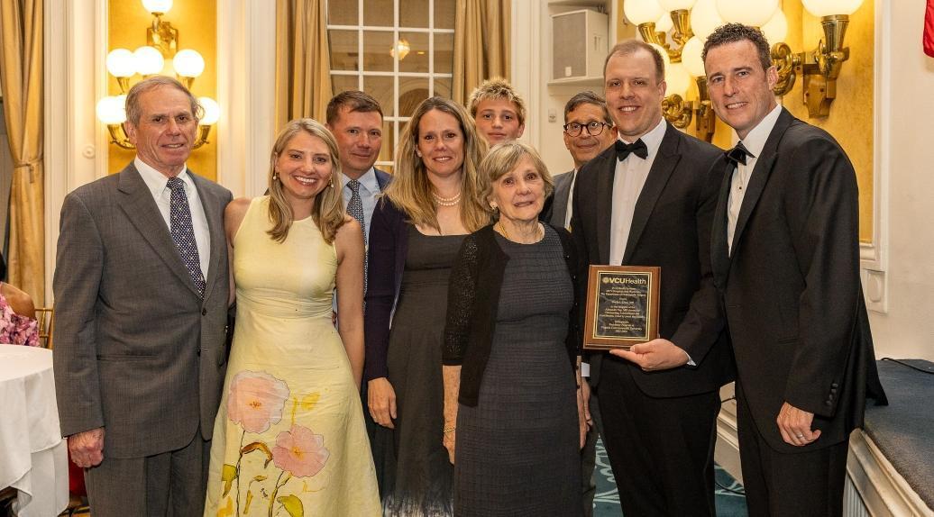 A group photo of nine people. The second man to the right is holding an award. 
