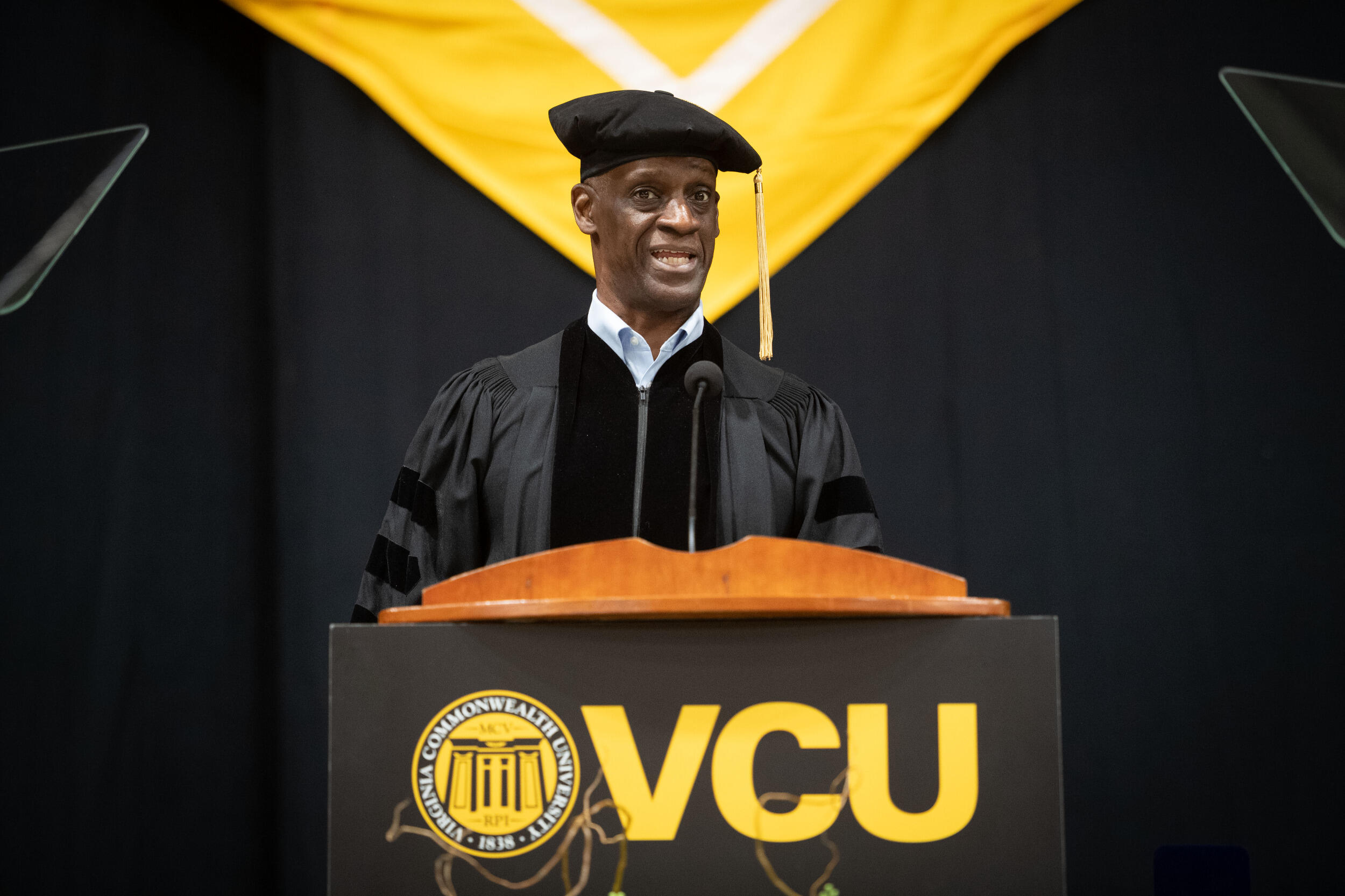 A man in cap and gown speaks behind a lectern.