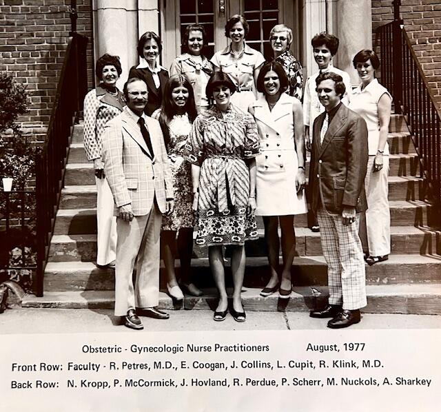 A black and white group photo of 12 people standing on the stair case in front of a building. Text reads \"Obstetric - Gynecologic Nurse Practitioners\" \"August, 1977\" \"Front Row: Faculty - R. Peters, M.D., E. Coogan, J. Collins, L, Cupit, R. Klink, M.D.\" \"Back Row: N. Kropp, P. McCormick, J. Holvand, R. Perdue, P. Scherr, M. Nucklos, A. Sharkey.\" 