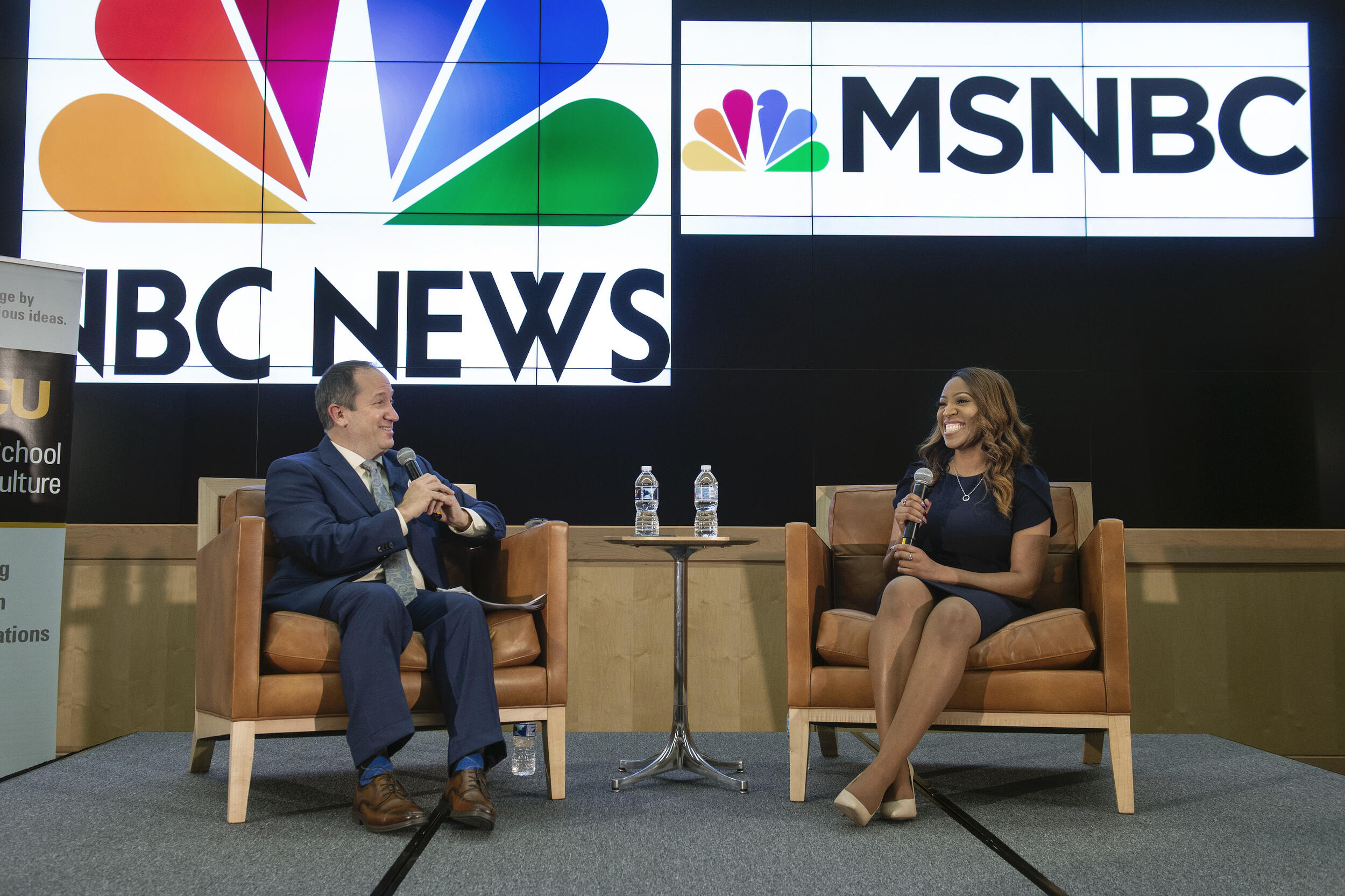 Tim Bajkiewicz, Ph.D., Chandelis Duster seated on a stage. Logos for NBC News and MSNBC are displayed on the screen behind.