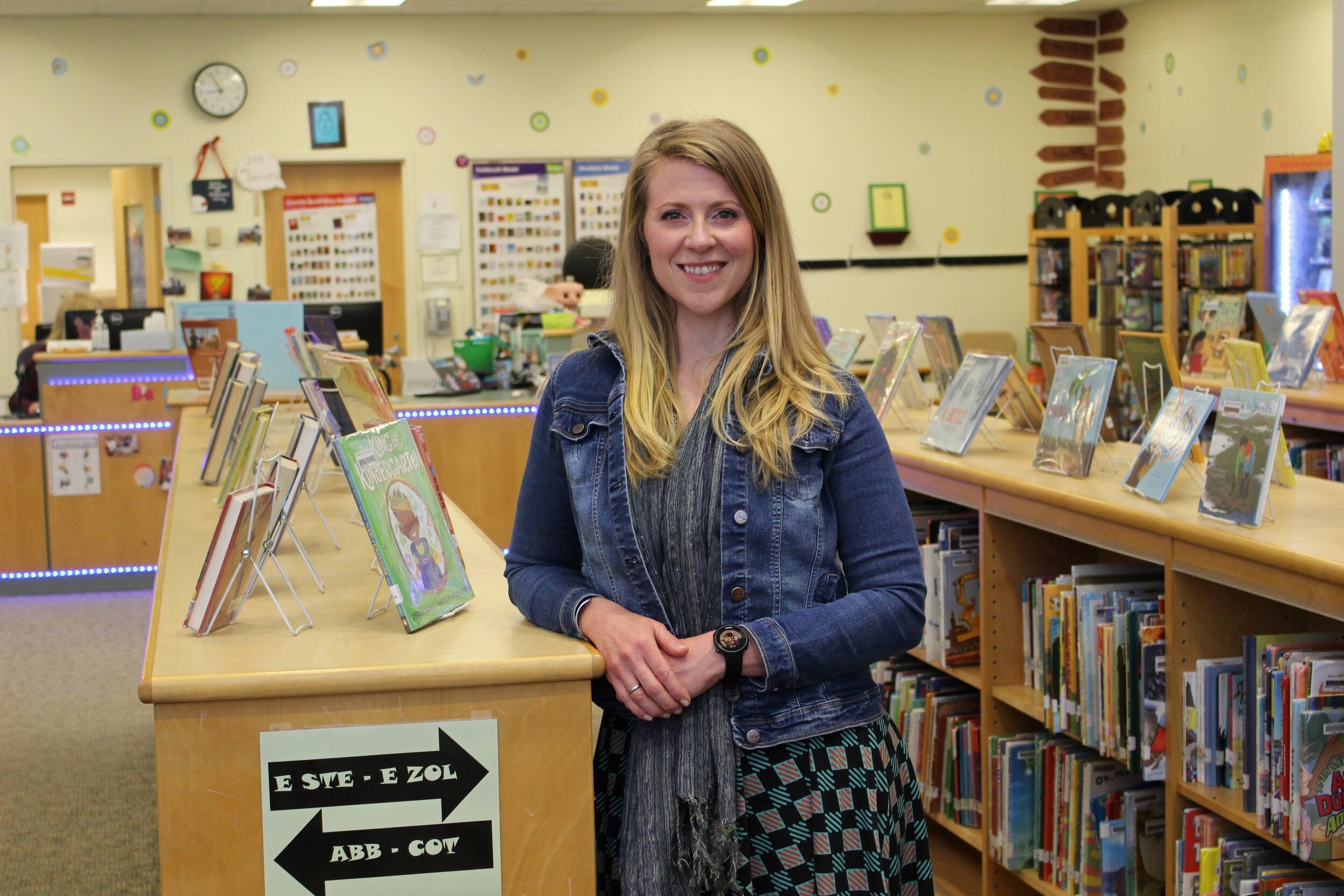 Holly Guelig leaning against a bookshelf in a grade school library 