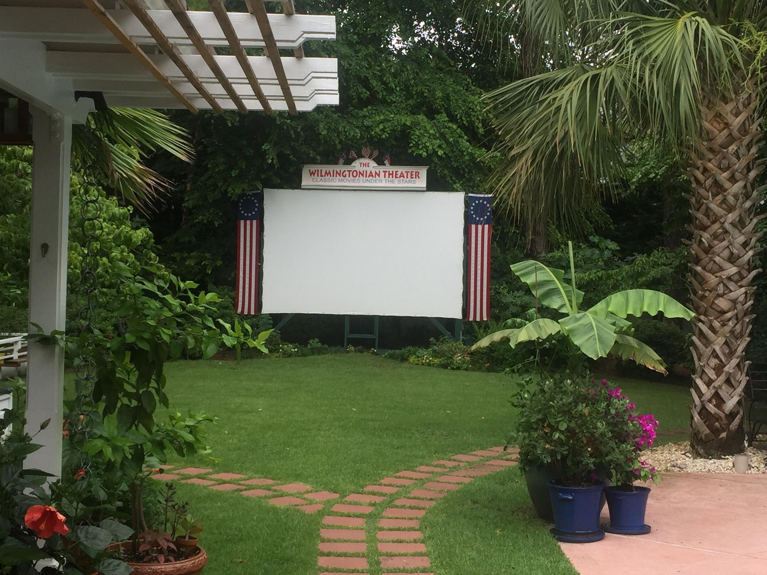A photo of a screen in a back yard with a sign over it that says \"WILMINGTONIAN THEATER\"