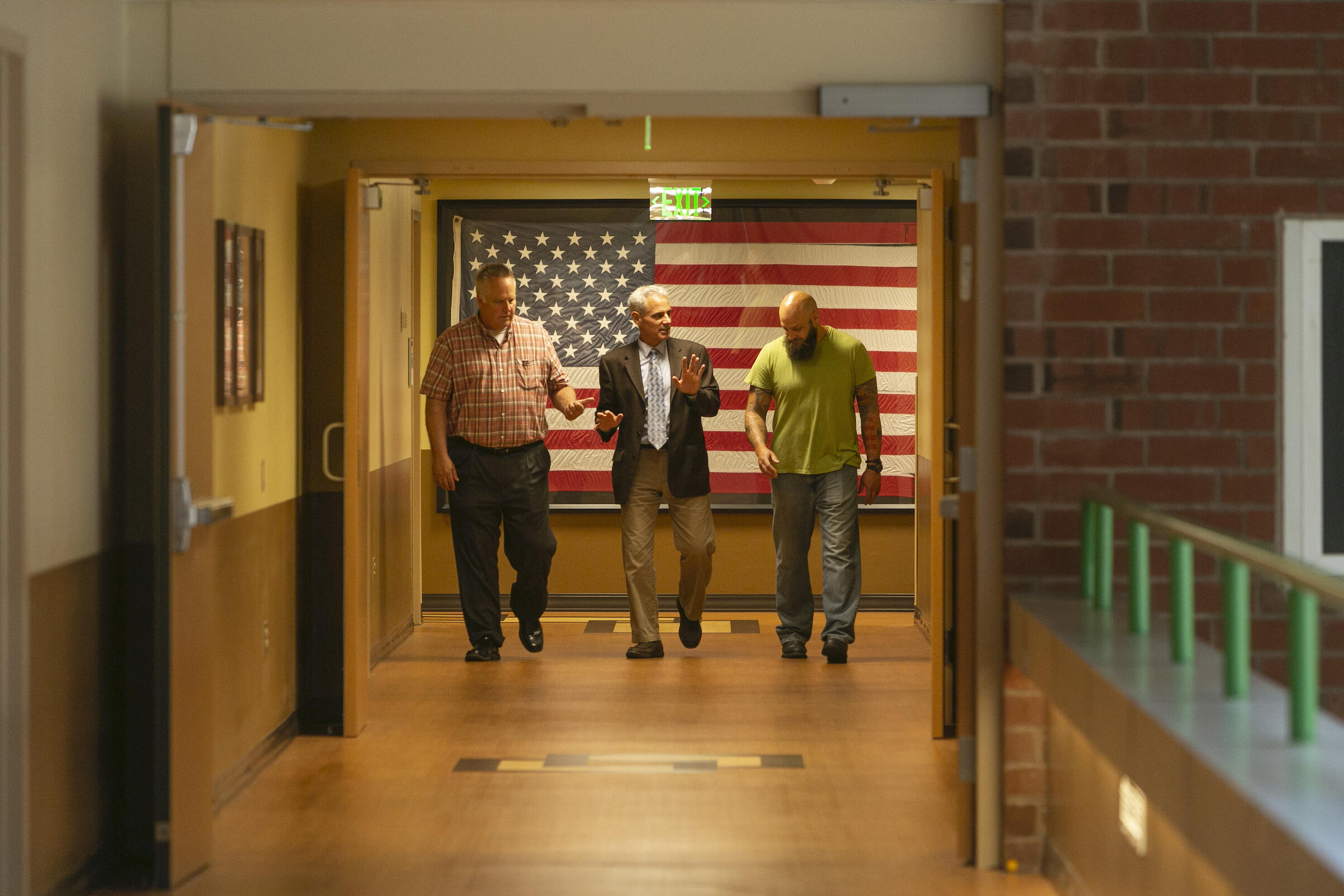 Three people walk down the corridor of a hospital. The flag of the United States is displayed behind them.