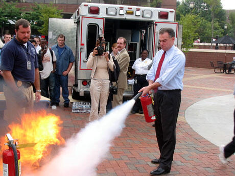 Governor Timothy M. Kaine practices using a fire extinguisher during the BYOB (Bring Your Own Batteries) interactive safety and preparedness fair at the Commons Plaza.   Troy Bower (left) is a fire safety inspector with the VCU Office of Environmental Health and Safety.  Bower reminded students to think PASS (pull, aim, squeeze and sweep) when they need to use a fire extinguisher.  Photo by Mike Porter/University News Services