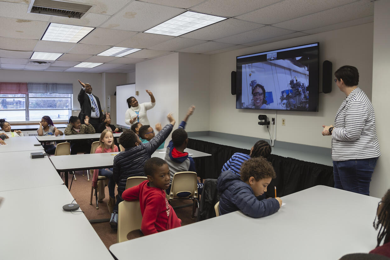 Students and instructors in a classroom participate in a video conference session.