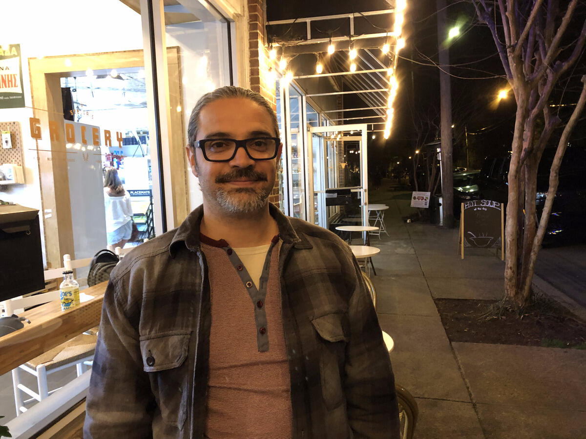 A man wearing glasses with a short beard standing outside at night. 