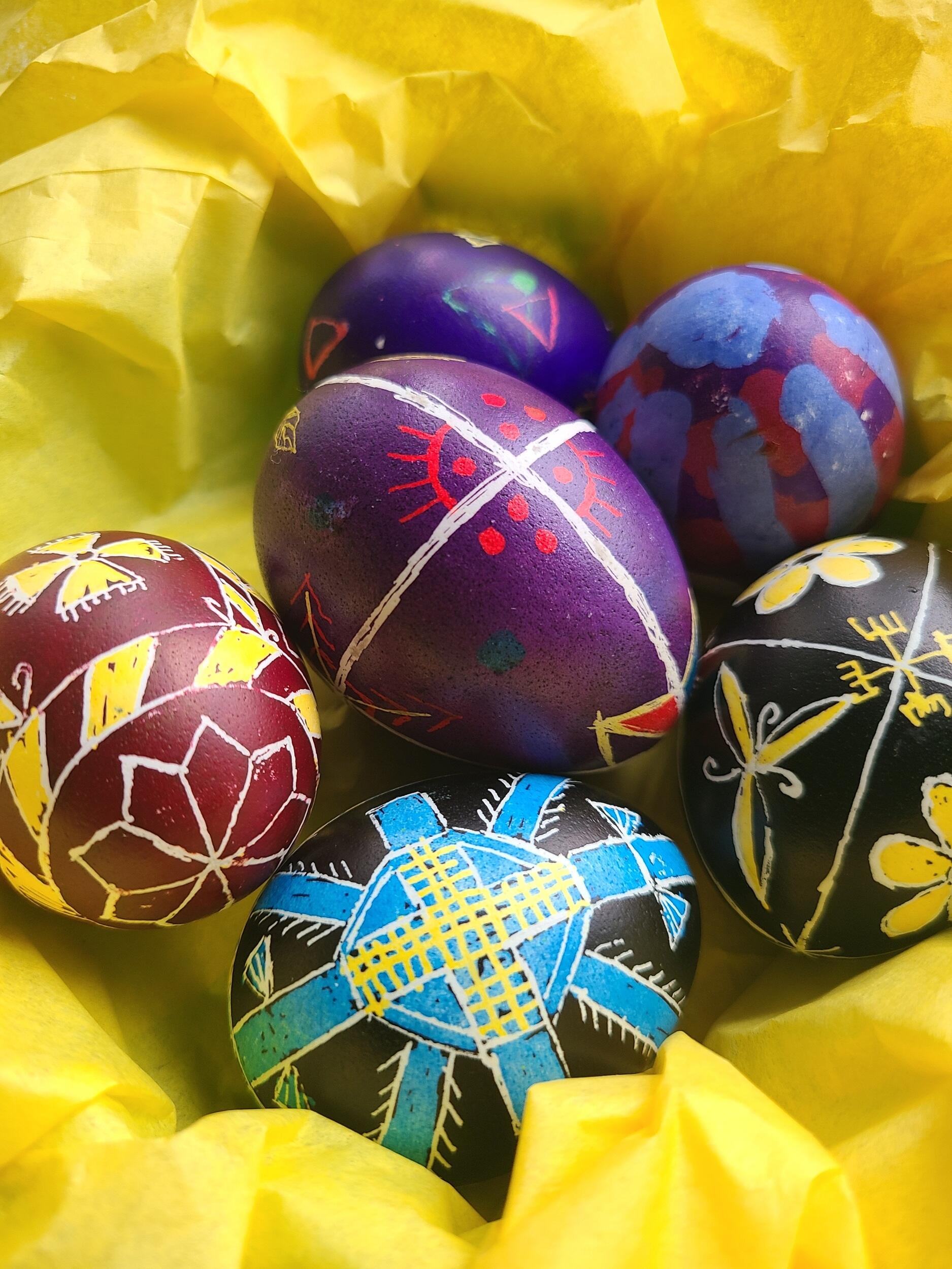 Five eggs with colorful patterns sitting on yellow tissue paper