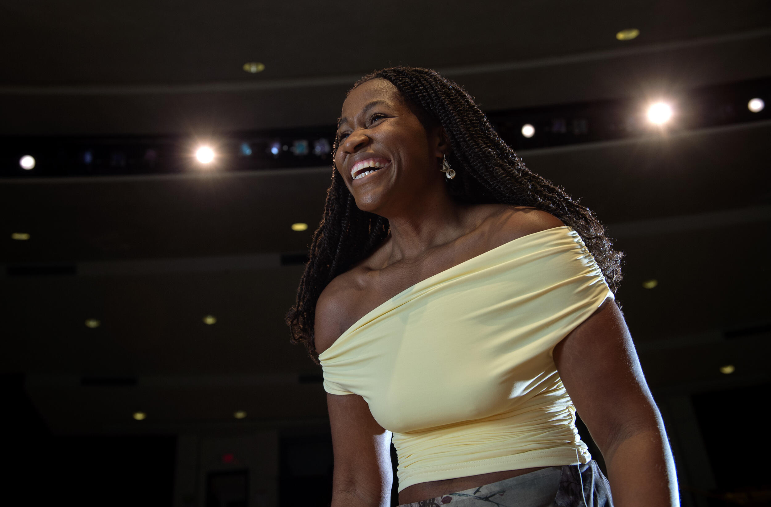 A photo of a woman from the chest up. She is smiling and wearing a yellow, off the shoulders shirt. 