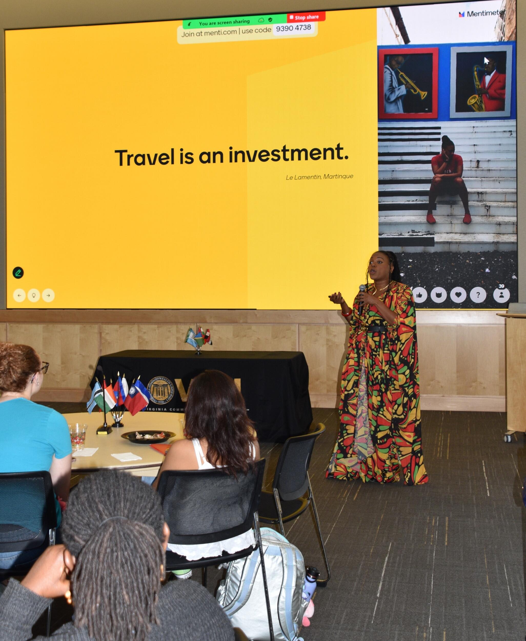 A photo of a woman speaking at the pront of a room. 