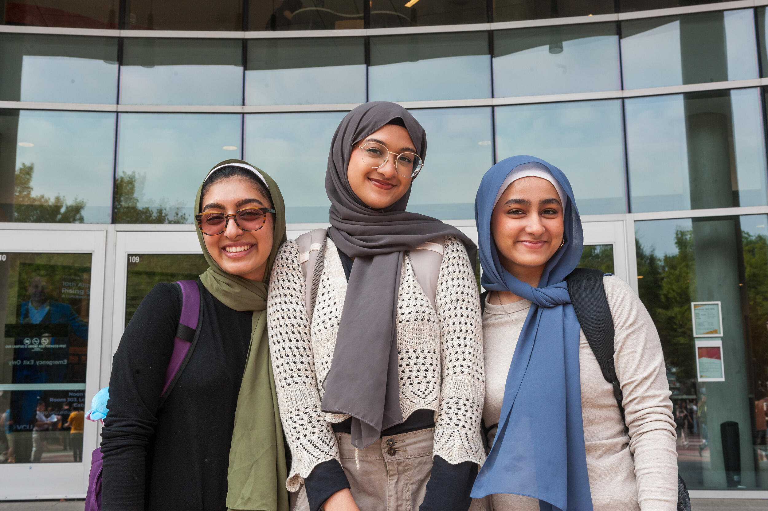 Three women wearing head scarves standing in front of the library. 